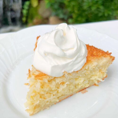 Slice of Impossible Coconut Pie on a plate, topped with whipped cream.