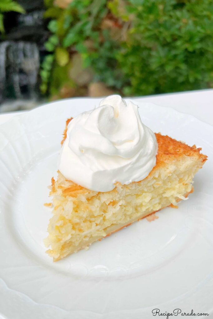 Slice of Impossible Coconut Pie on a plate, topped with whipped cream.