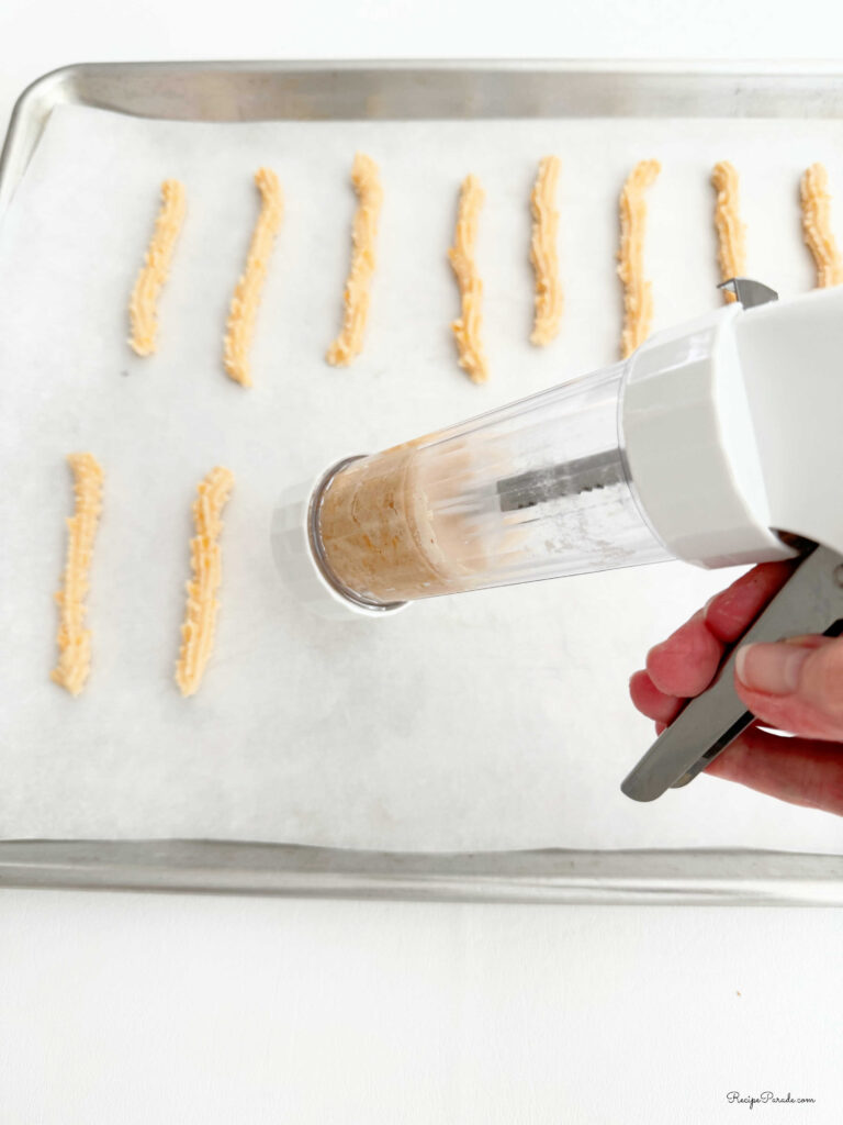 Using cookie press to pipe the cheese straws on a cookie sheet.