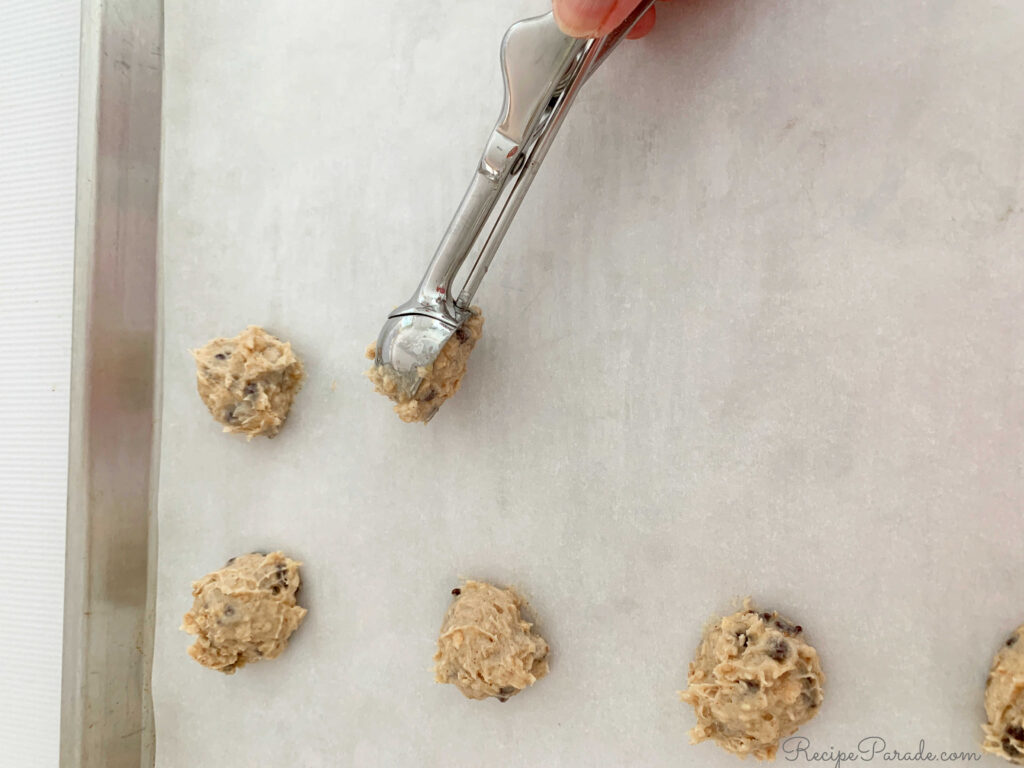 Dropping spoonfuls of cookie dough onto a parchment lined cookie sheet.