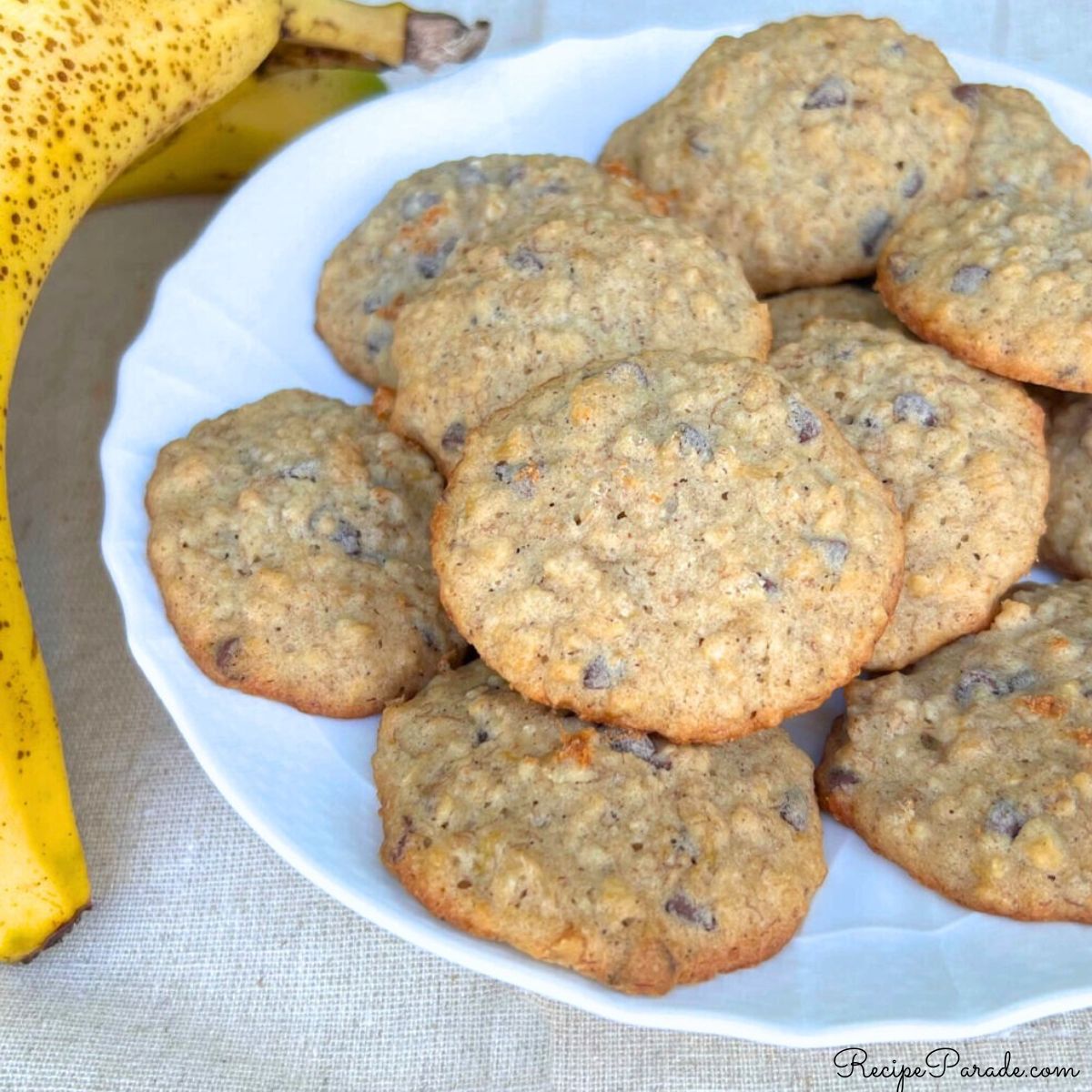 Banana Oatmeal Chocolate Chip Cookies on a white plate, with a banana next to it.