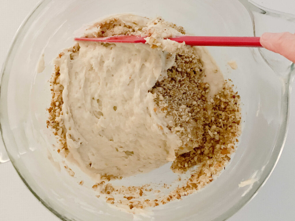 Folding the chopped pecans and mashed bananas into the banana bread batter.