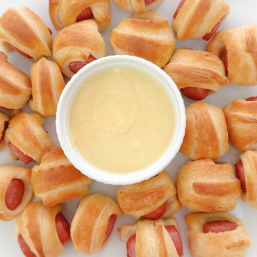 Pigs in a blanket bites on a platter with sauce.
