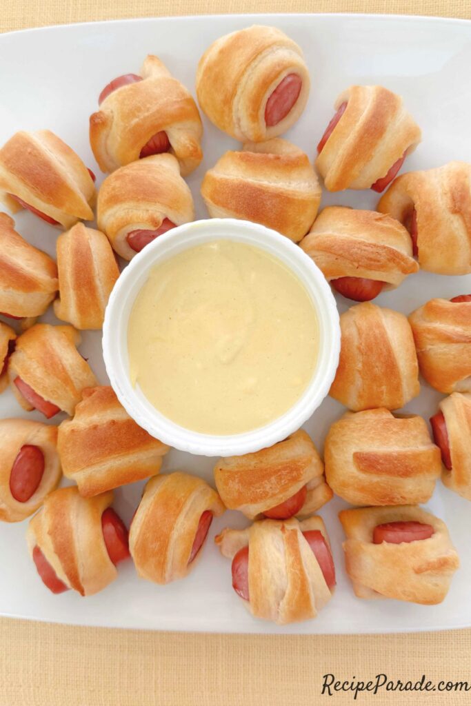 Pigs in a blanket bites on a platter with sauce.