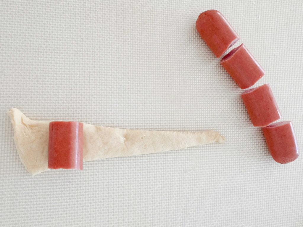 Rolling hot dogs (sliced into fourths) into crescent roll dough.