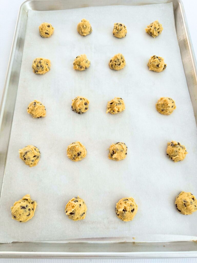Balls of chocolate chip cookie dough on a parchment lined cookie sheet.