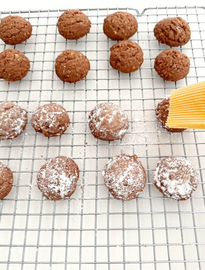 Brushing the warm Chocolate Mexican Wedding Cookies with powdered sugar using a pastry brush.